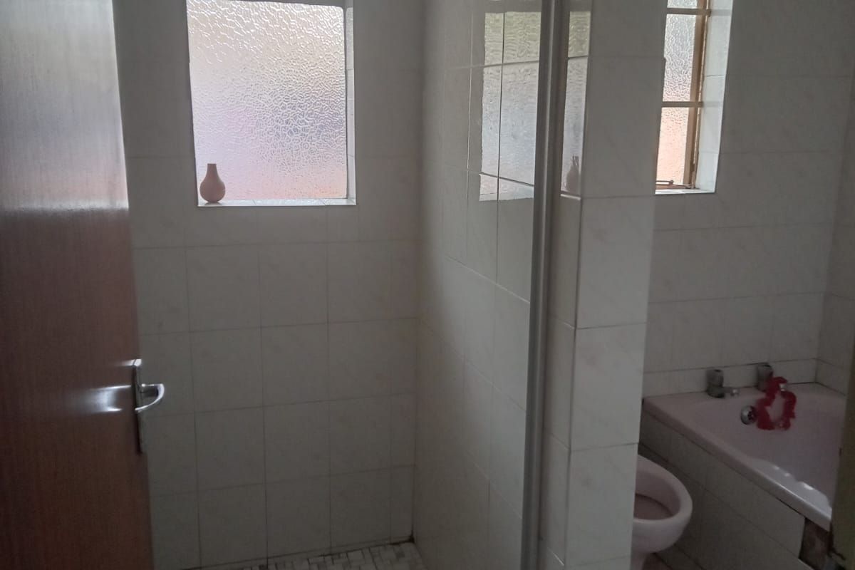 A functional bathroom featuring a walk-in shower with a glass partition, a bathtub, and tiled walls. The shower floor requires repair.