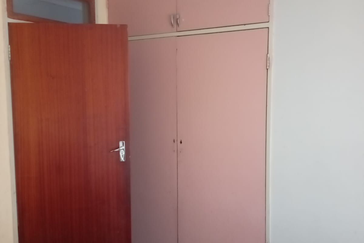 A bedroom featuring built-in cupboards with a dated finish and a wooden door, providing basic storage and access.