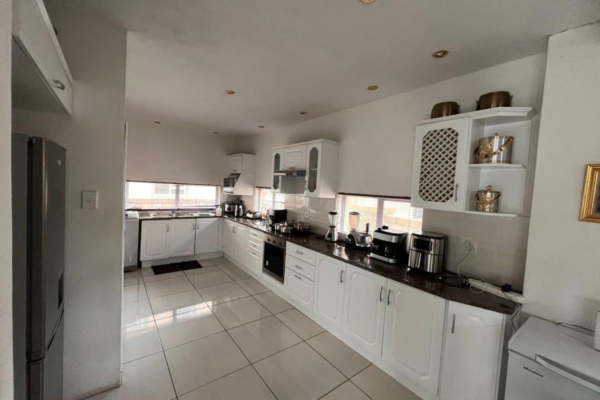 A functional kitchen featuring white cabinetry, dark granite countertops, tiled flooring, and built-in appliances including an oven and extractor fan.