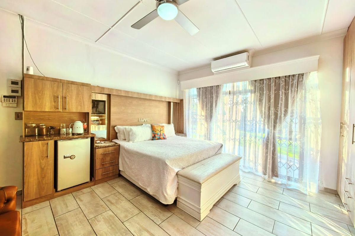 Spacious bedroom featuring built-in wooden cabinetry, integrated mini-fridge station, ceiling fan, wall-mounted air conditioning unit, and large sliding glass doors leading to the exterior.