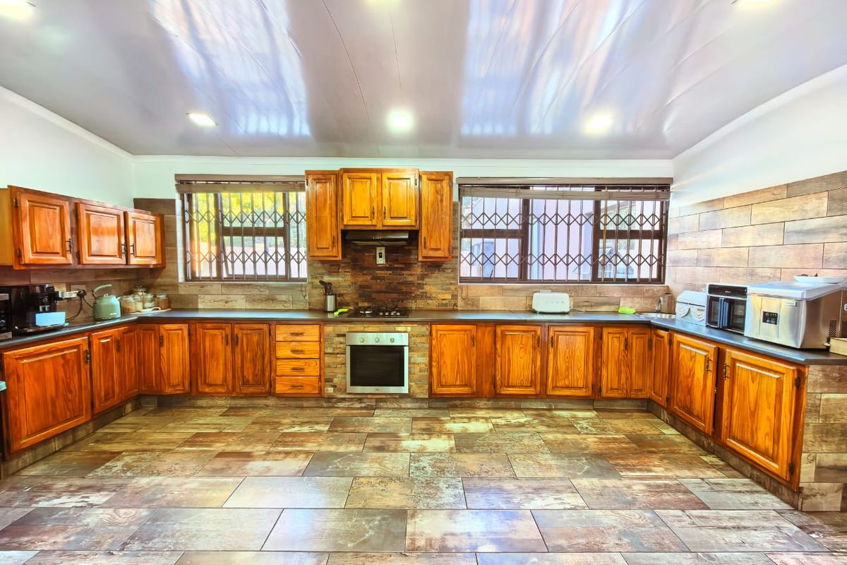 Spacious kitchen featuring extensive wooden cabinetry, built-in oven and hob, stone-look tiled flooring, and large windows with security bars.