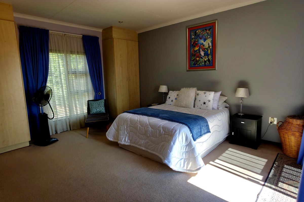 A spacious bedroom featuring built-in wooden cupboards, neutral carpeting, and large windows that allow for natural light.