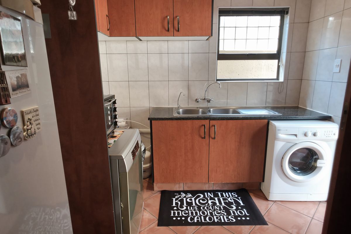 A functional kitchen featuring wooden cabinetry, tiled splashbacks, a double sink, and dedicated space for a washing machine.