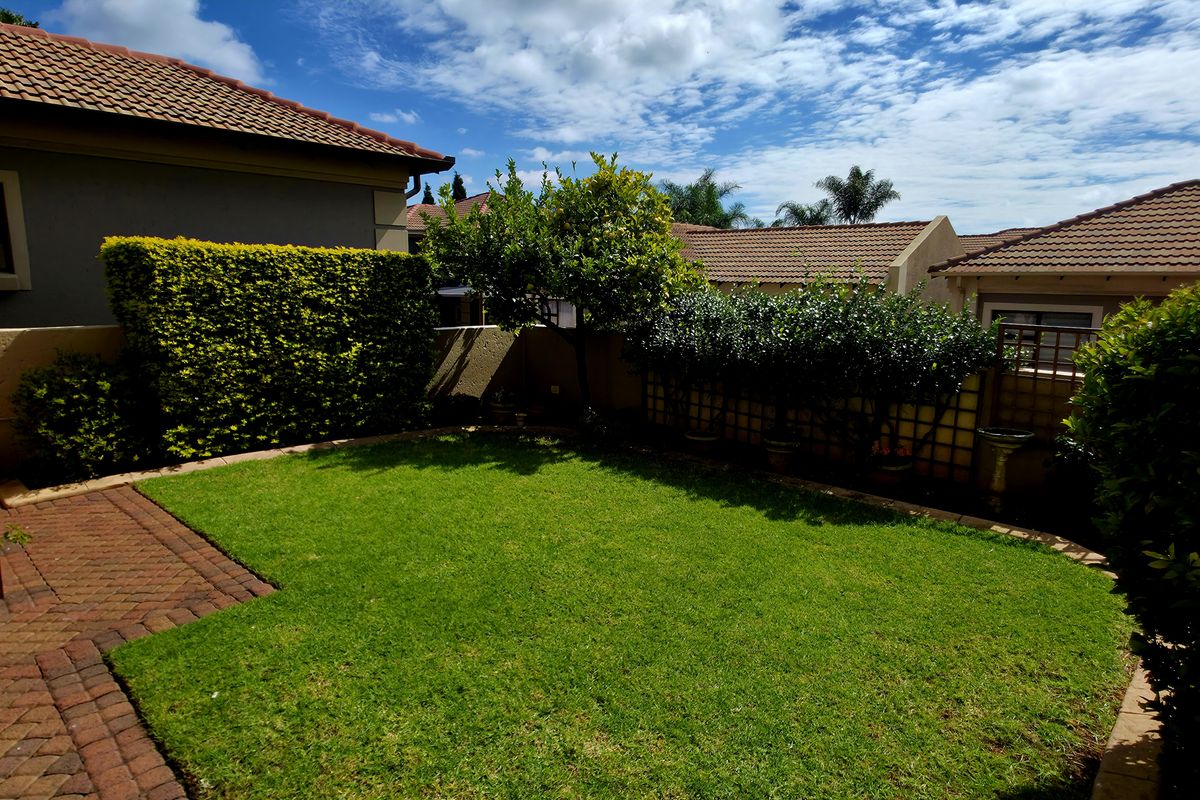 A private rear garden featuring a well-maintained lawn, paved patio area, and established perimeter hedging, providing a peaceful outdoor space.