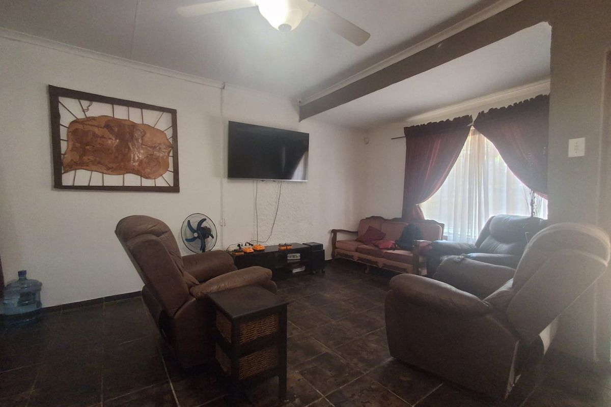 A living room featuring tiled flooring, a ceiling fan, and a large window with curtains, providing a functional and comfortable space.