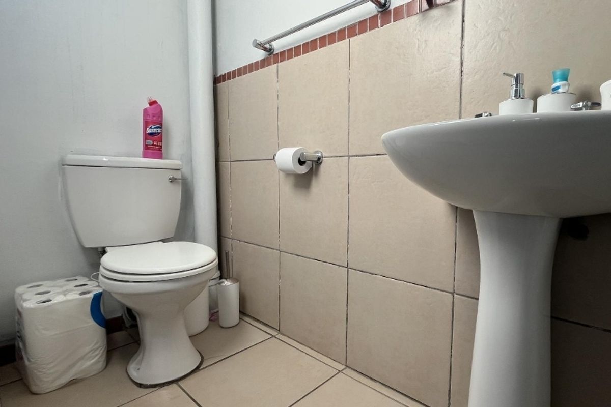 A functional bathroom featuring a pedestal sink, a standard toilet, and tiled walls with a decorative border.