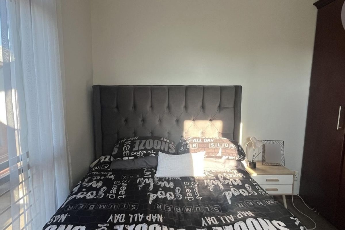 A well-lit bedroom featuring a built-in wardrobe and large window with sheer curtains, providing a comfortable and functional living space.