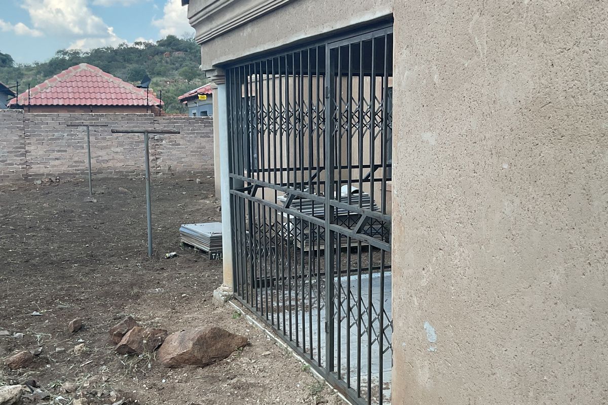 View of the rear exterior of the property featuring a security gate, concrete flooring, and an undeveloped backyard area.