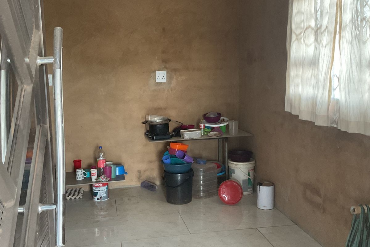A small, unfinished utility or kitchen space featuring tiled flooring and basic wall finishes, currently used for storage.