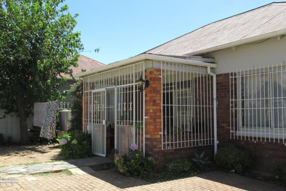 A view of the rear exterior of the house featuring a covered patio area with security bars and paved outdoor space.