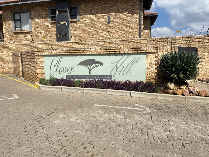 The entrance facade of Clover Hill townhouse complex, featuring face-brick construction, paved driveway, and landscaped signage wall.
