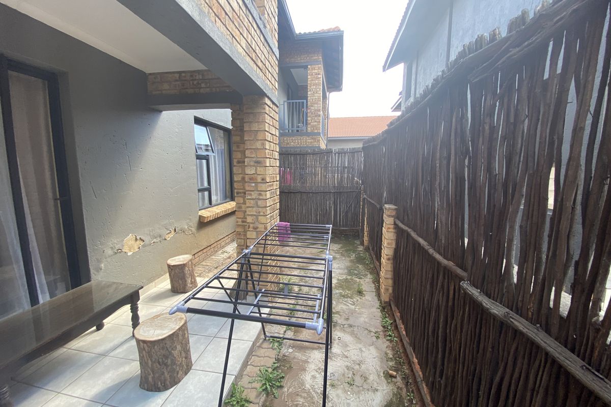 A side exterior area of the townhouse featuring tiled patio space, brick pillars, and a rustic stick fence boundary.