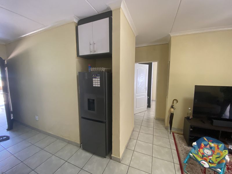 Interior view of a tiled living area featuring a built-in overhead storage cabinet and access to a hallway.