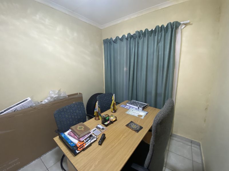A small room currently utilized as a home office, featuring tiled flooring and a window with curtain fixtures.