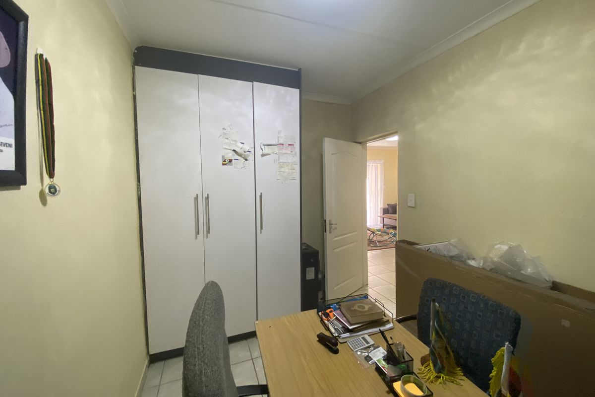A functional bedroom featuring built-in cupboards and tiled flooring, offering a practical space with direct access to the adjacent living area.