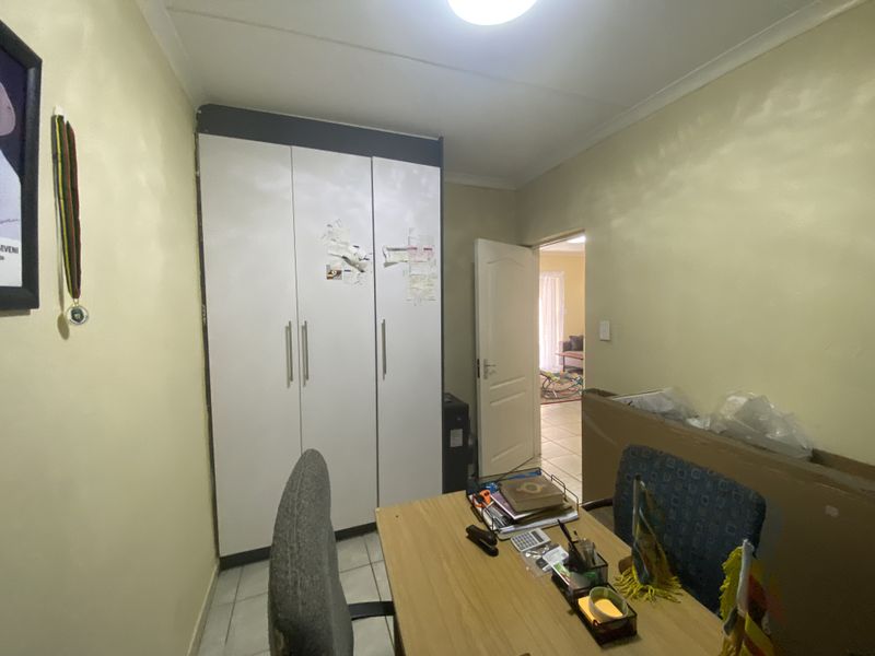 A functional bedroom featuring built-in cupboards and tiled flooring, offering a practical space with direct access to the adjacent living area.