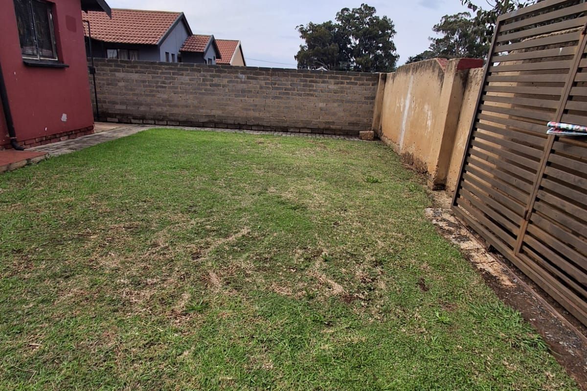 A private rear garden area featuring a lawn, enclosed by a combination of brick and concrete boundary walls and a wooden privacy screen.