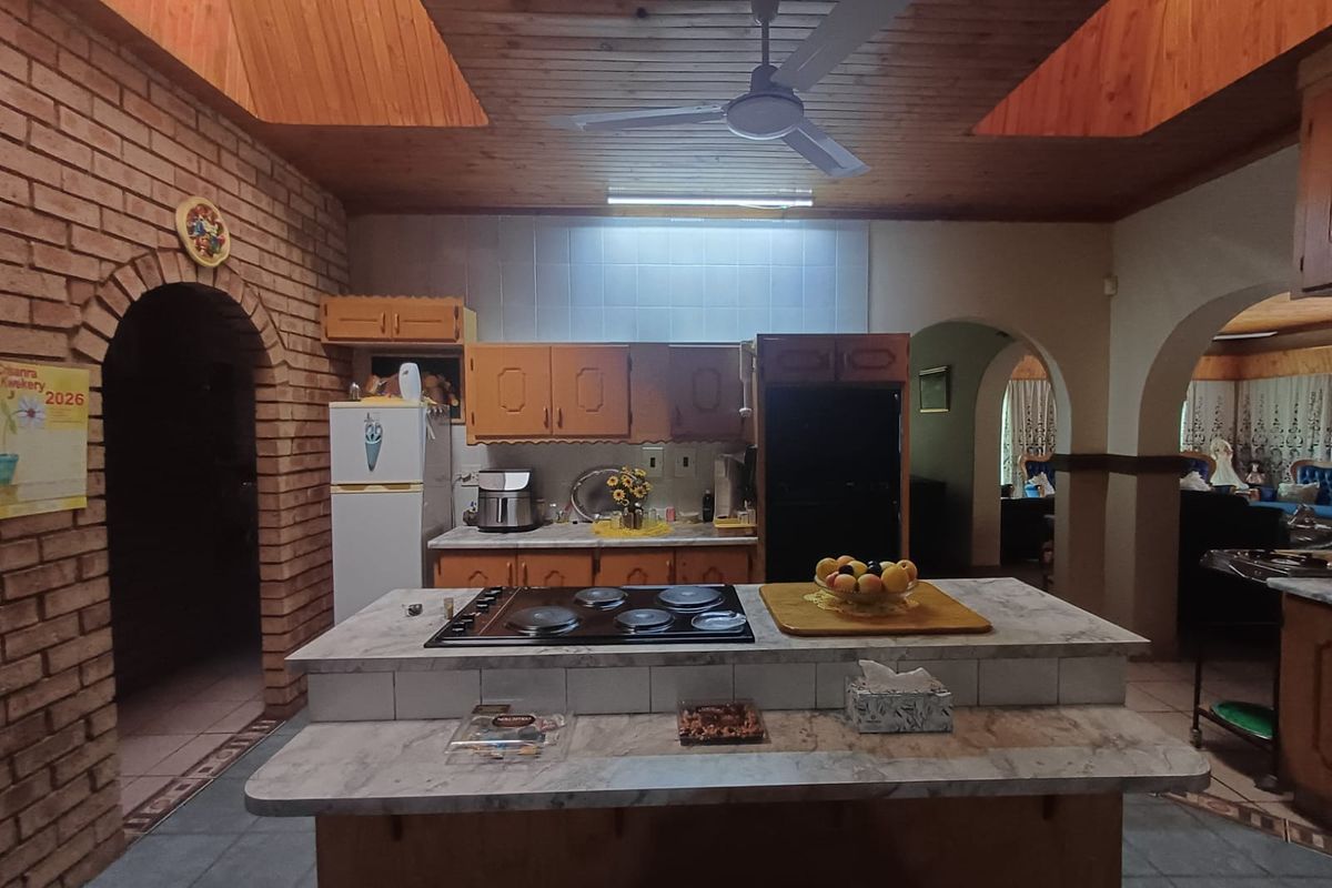 Spacious kitchen featuring a central island with a built-in hob, exposed brickwork, and a timber-clad vaulted ceiling with a ceiling fan.