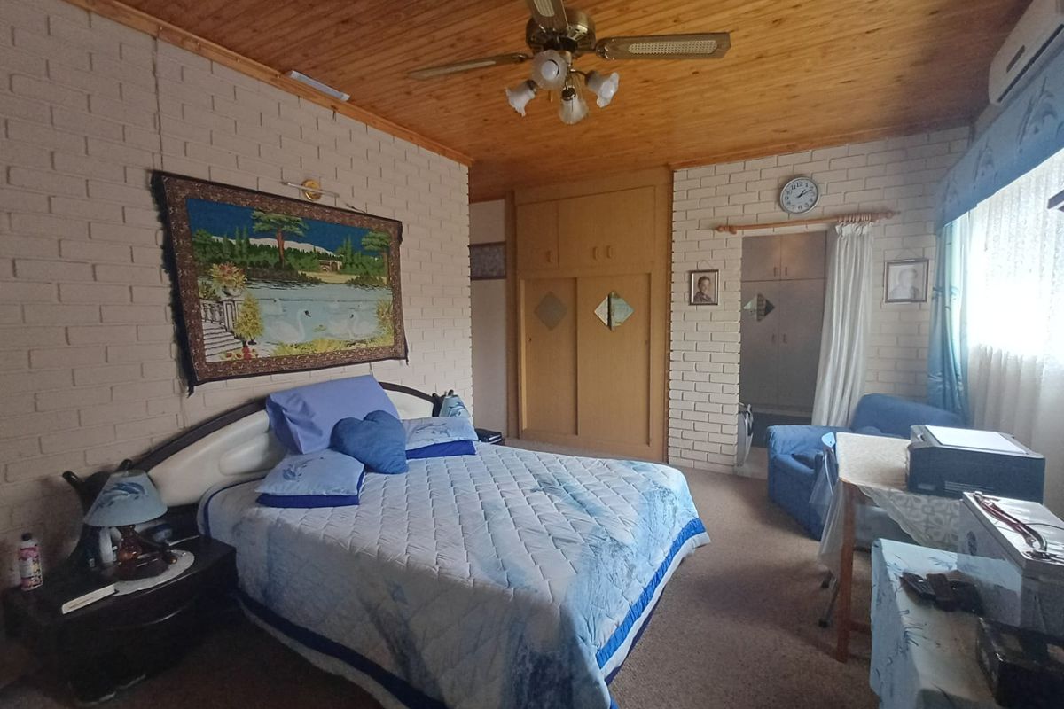 Spacious bedroom featuring exposed brick walls, built-in wooden cupboards, a ceiling fan, and an attached walk-in closet area.
