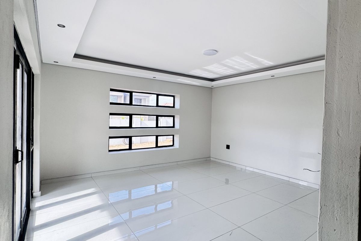 A bright, modern, and spacious living area featuring large white floor tiles, recessed ceiling lighting, and expansive glass sliding doors leading outdoors.