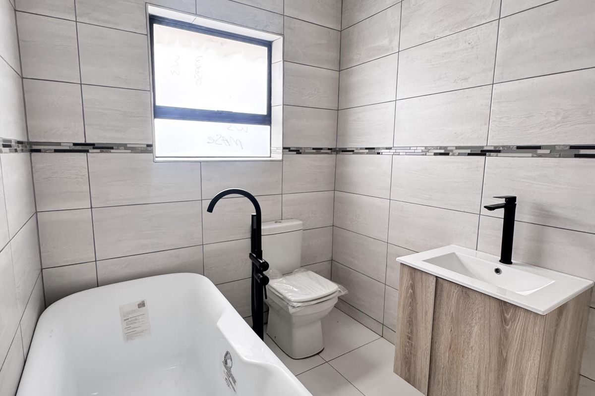 Modern bathroom featuring a freestanding bathtub, wall-mounted vanity with basin, matte black fixtures, and neutral floor-to-ceiling wall tiles.