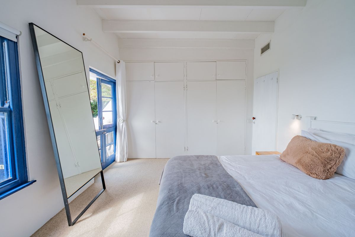 Bright bedroom featuring built-in cupboards, exposed ceiling beams, and direct access to an outdoor area through a blue-framed door.