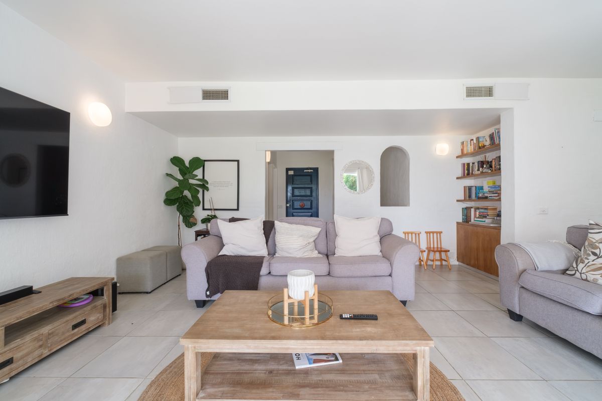 A bright living room featuring tiled flooring, built-in shelving, and ducted air conditioning vents, creating a comfortable and functional space.