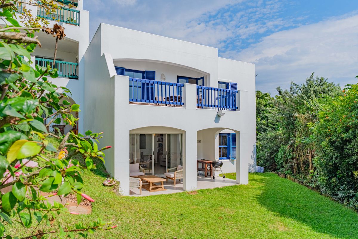 Rear view of a townhouse featuring a ground floor covered patio, an upper-level balcony with blue balustrades, and a well-maintained private garden.