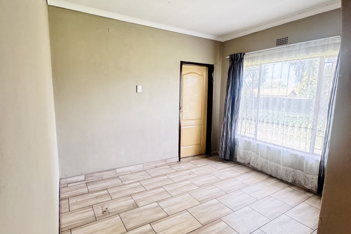 A bright, empty bedroom featuring wood-look ceramic floor tiles, a large window with security bars, and a neutral color palette.