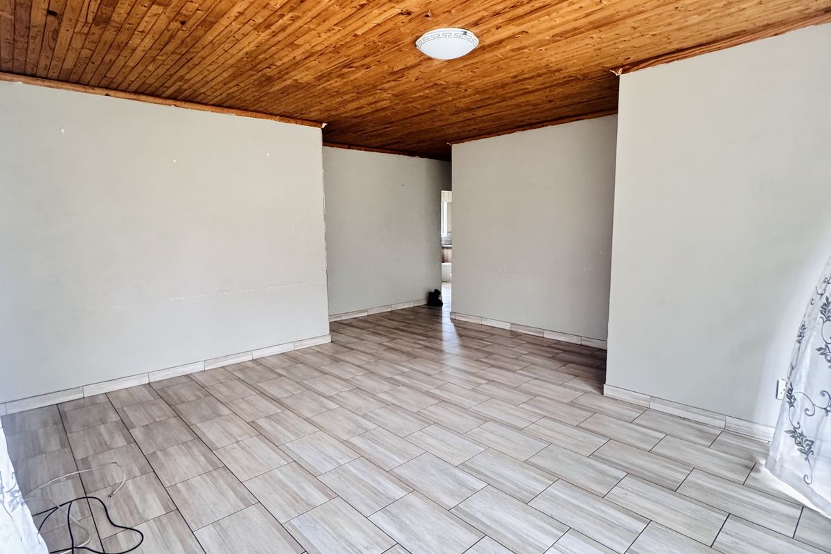 An empty living area featuring light-toned wood-look floor tiles and a natural timber-clad ceiling, offering a neutral canvas for interior design.