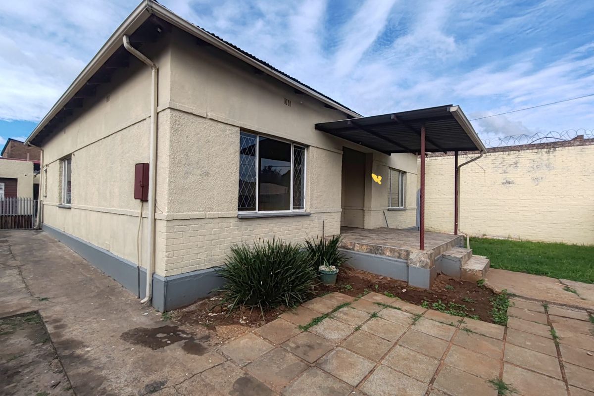 Rear view of the property featuring a covered patio, paved outdoor area, and a secure perimeter wall with security spikes.