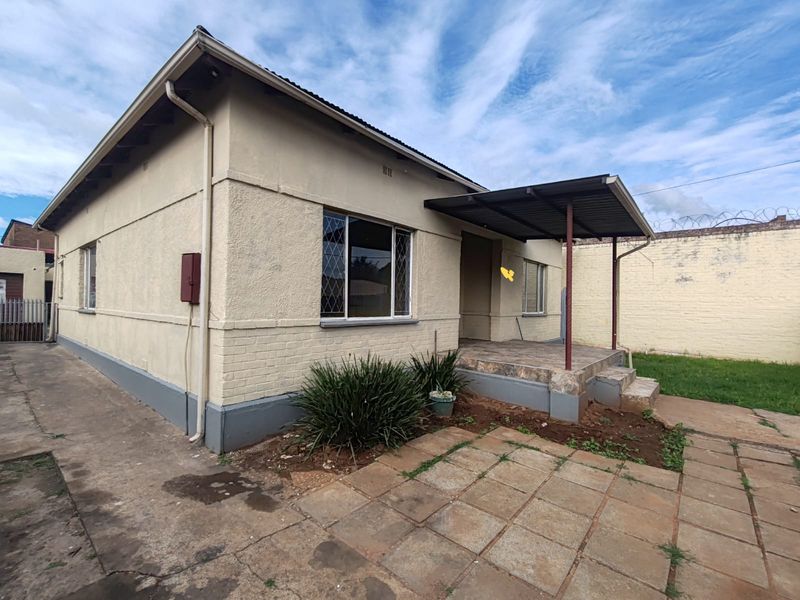 Rear view of the property featuring a covered patio, paved outdoor area, and a secure perimeter wall with security spikes.