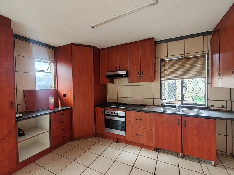A functional kitchen featuring wood-look cabinetry, built-in oven and hob, double sink, and tiled finishes, offering a blank canvas for modern renovation.