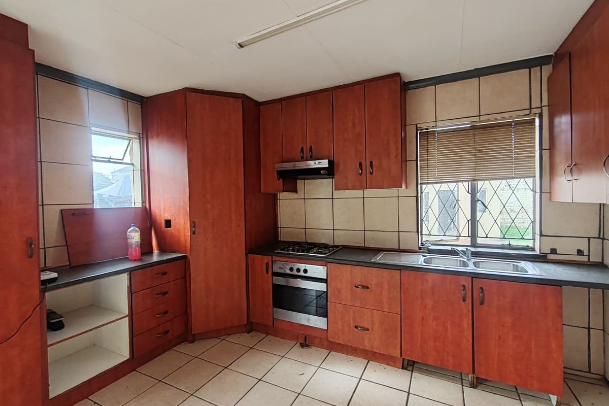 A functional kitchen featuring wood-look cabinetry, built-in oven and hob, double sink, and tiled finishes, offering a blank canvas for modern renovation.