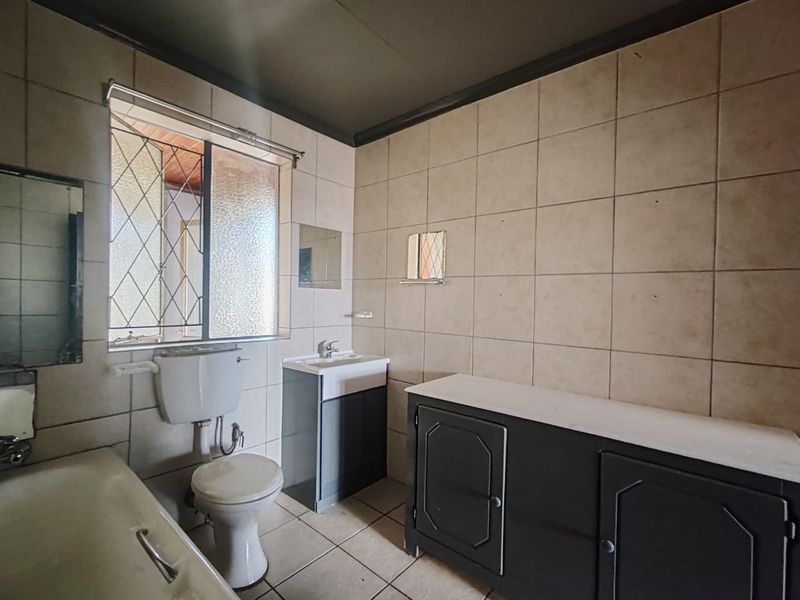 A dated bathroom featuring a bathtub, toilet, and vanity cabinet with neutral wall and floor tiling.