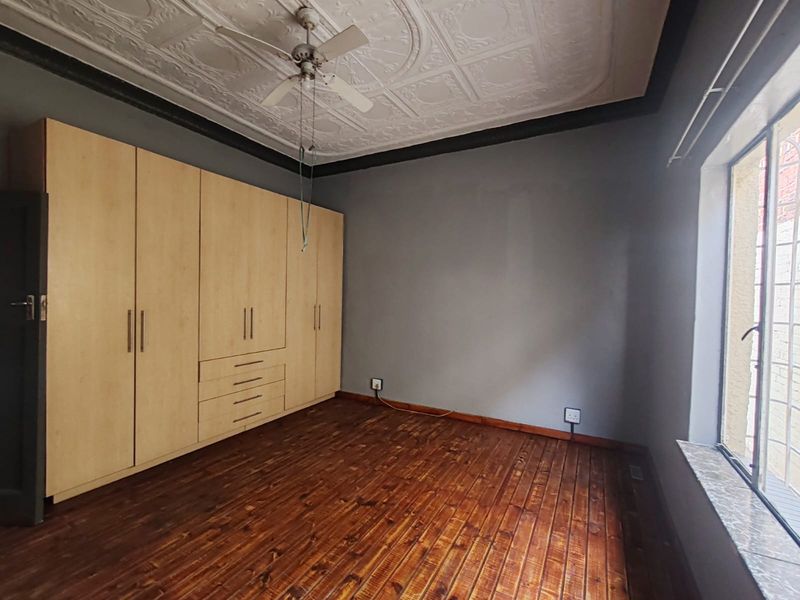 A bedroom featuring original pressed metal ceilings, built-in wooden cabinetry, and polished timber flooring with a window fitted with security bars.