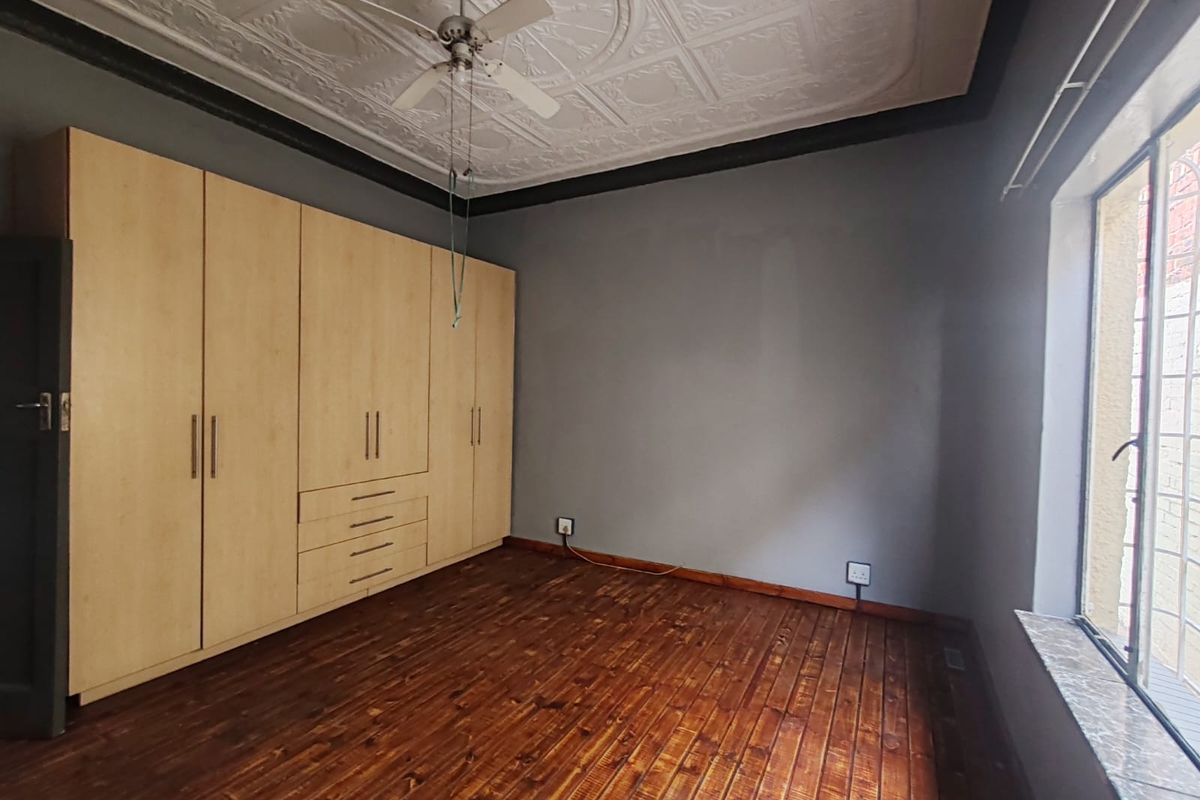 A bedroom featuring original pressed metal ceilings, built-in wooden cabinetry, and polished timber flooring with a window fitted with security bars.