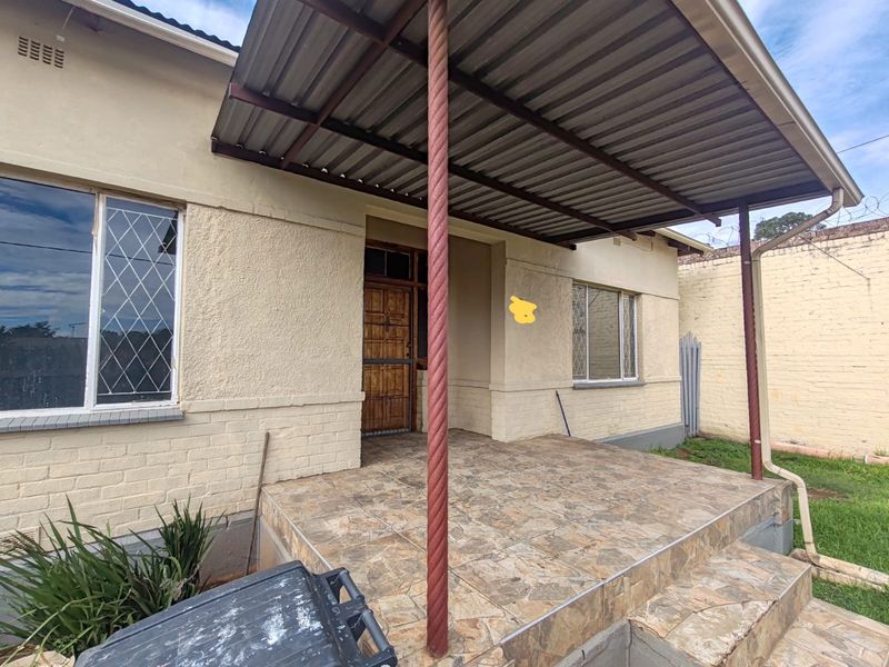 A covered outdoor patio area featuring tiled flooring, metal support columns, and a timber entrance door, providing a functional space for outdoor relaxation.
