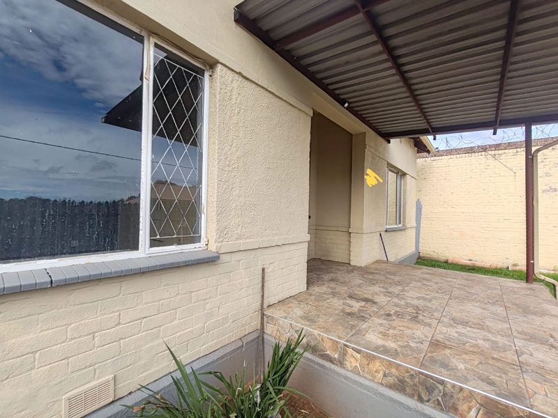 A covered outdoor patio area featuring tiled flooring, metal roofing, and security features, providing a functional space for outdoor relaxation.