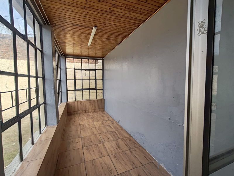 An enclosed patio or sunroom featuring timber-look tiled flooring, a timber-clad ceiling, and large steel-framed windows overlooking the exterior.