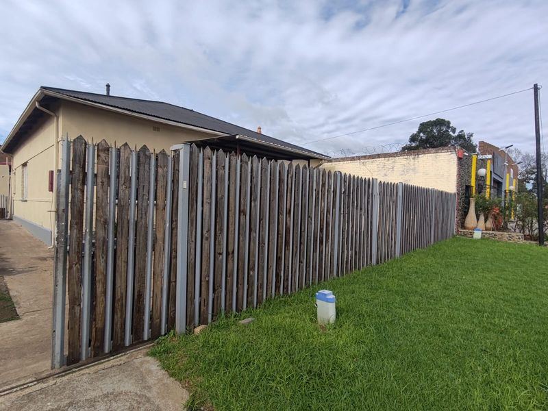 Exterior view of the property featuring a timber picket fence, concrete driveway, and lawn area with visible wear to the building facade.