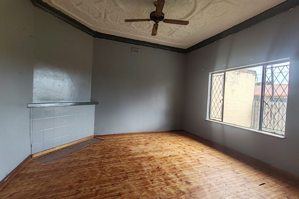 An empty living room featuring original ornate pressed metal ceilings, timber flooring, and a tiled fireplace, offering a blank canvas for renovation.