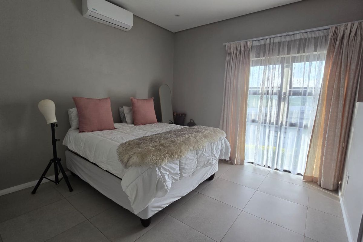 A well-maintained bedroom featuring neutral tiled flooring, a wall-mounted air conditioning unit, and large glass sliding doors providing natural light.