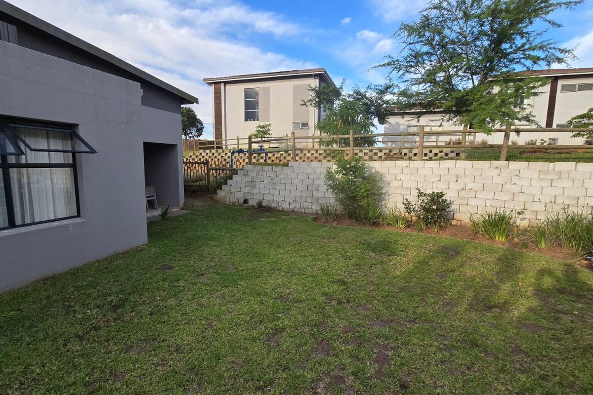 A private rear garden area featuring a grass lawn, concrete block retaining wall, and timber fencing, adjacent to the townhouse exterior.