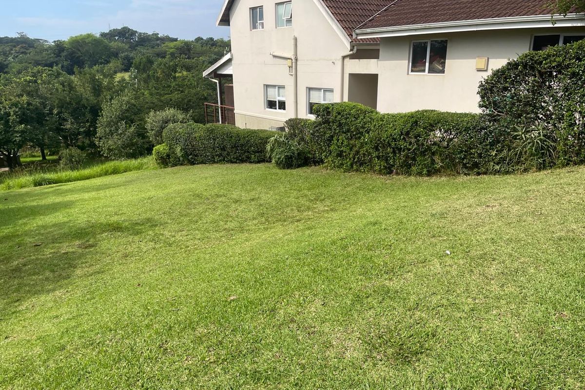 A view of the rear garden area featuring a well-maintained lawn, established hedges, and a partial view of the residential building exterior.