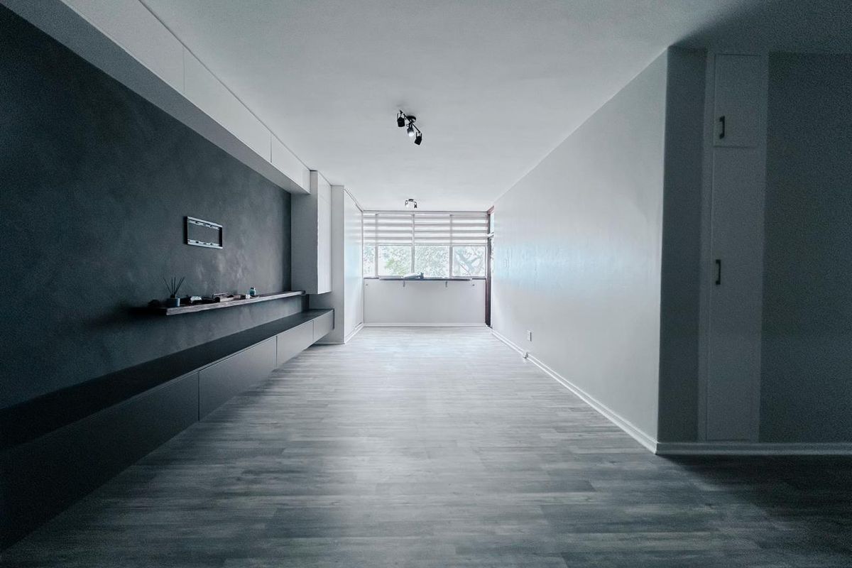 A spacious, empty living area featuring modern grey laminate flooring, a built-in dark feature wall with integrated shelving, and neutral white walls.