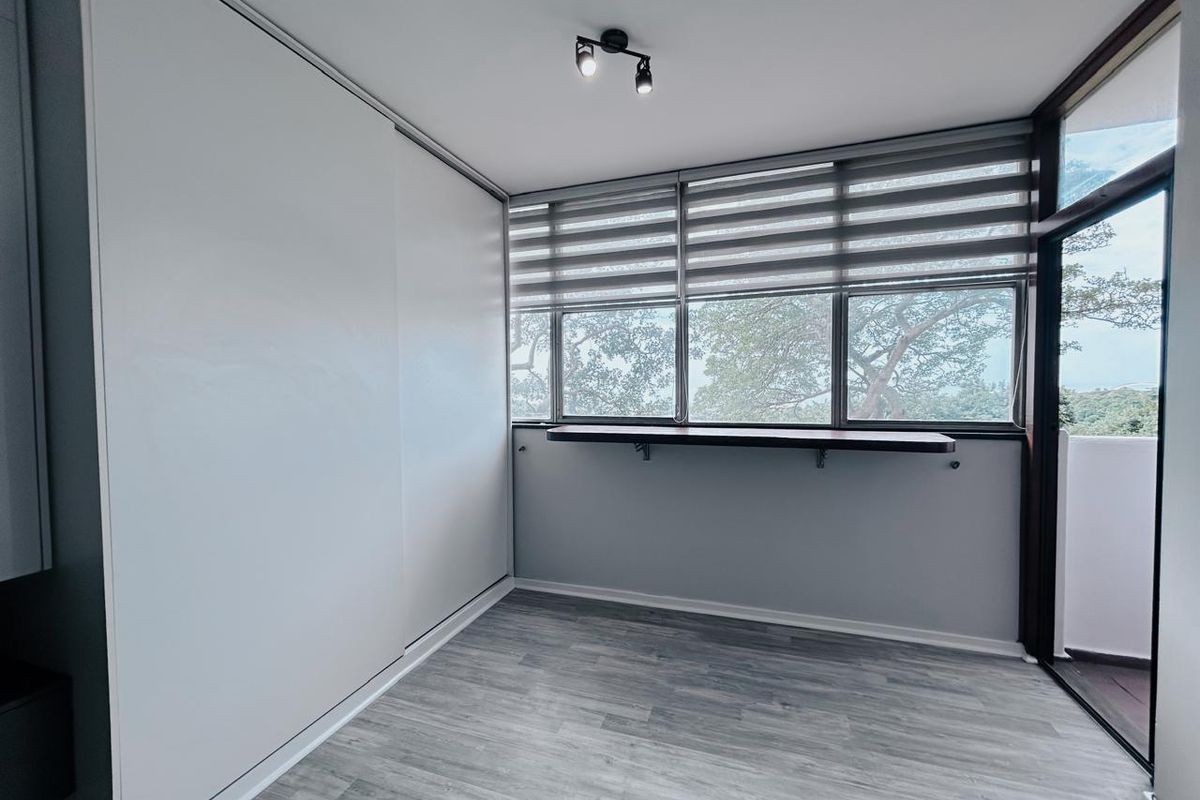 A bright bedroom featuring modern grey wood-look flooring, a large built-in sliding wardrobe, and a window-side breakfast bar with views.