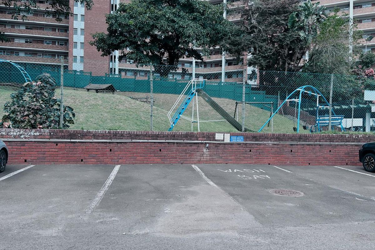 Outdoor parking area featuring a designated wash bay, adjacent to a communal playground with a slide and swing set within the apartment complex grounds.