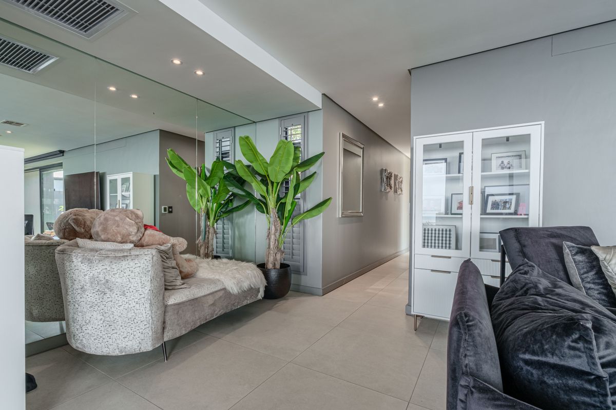 A modern living area featuring large wall-to-wall mirrors, recessed ceiling lighting, ducted air conditioning vents, and neutral floor tiling.