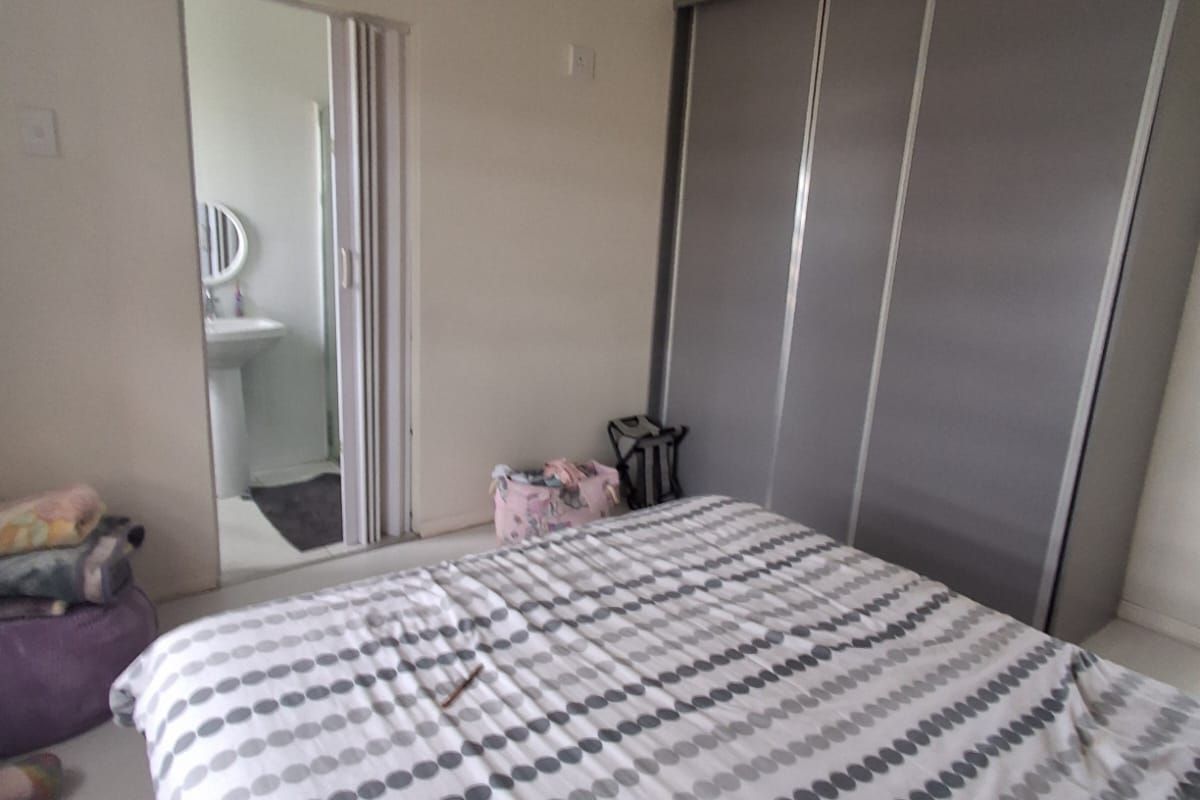 A bedroom featuring built-in sliding door cupboards and an adjoining en-suite bathroom with a pedestal basin.